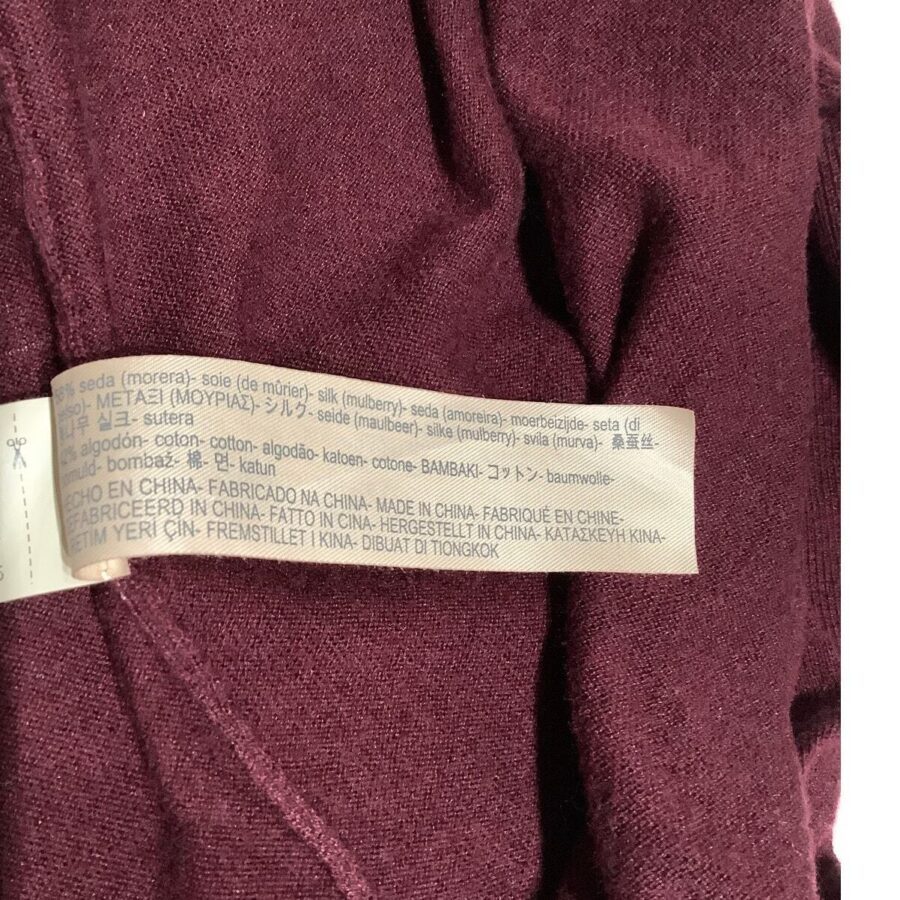 A burgundy fabric with a tag displaying care instructions and composition in multiple languages, indicating it is made of silk and cotton and manufactured in China.