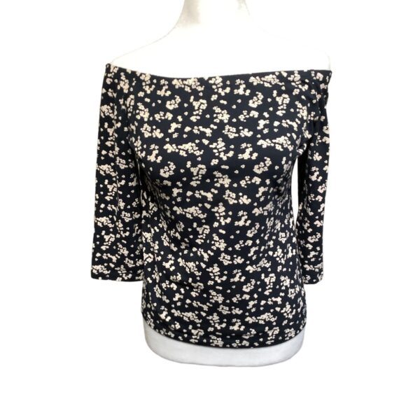 A black long-sleeve off-the-shoulder top with a white floral pattern displayed on a torso mannequin against a plain white background.