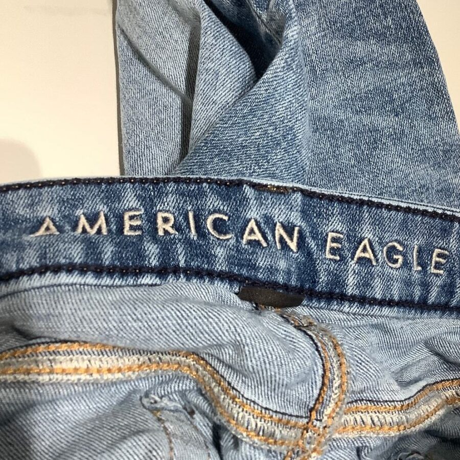 A close-up of light blue denim jeans with "American Eagle" embroidered on the waistband, showcasing detailed stitching and fabric texture.