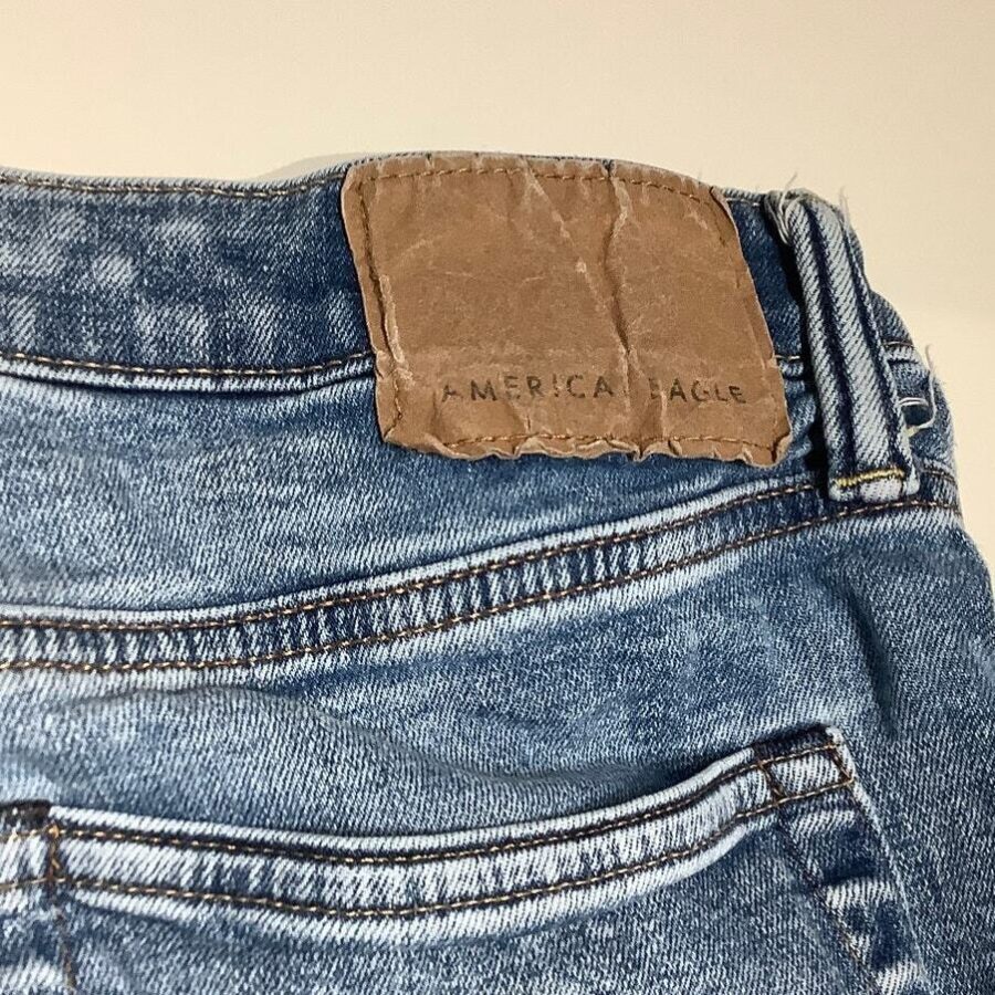 Close-up image of a pair of blue denim jeans with a brown, partially worn "American Eagle" label on the waistband.