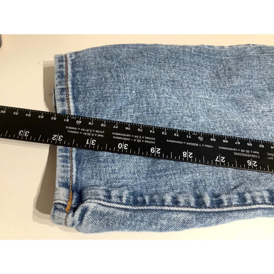 A black ruler measuring a folded piece of light blue denim fabric on a white surface, indicating a length of about 25 inches.