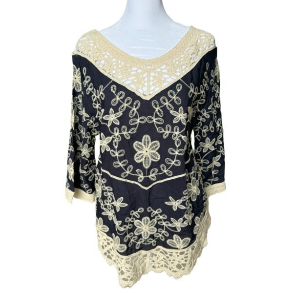 Intricate black and beige lace blouse displayed on a mannequin, featuring floral and geometric patterns with a V-neck and three-quarter length sleeves.