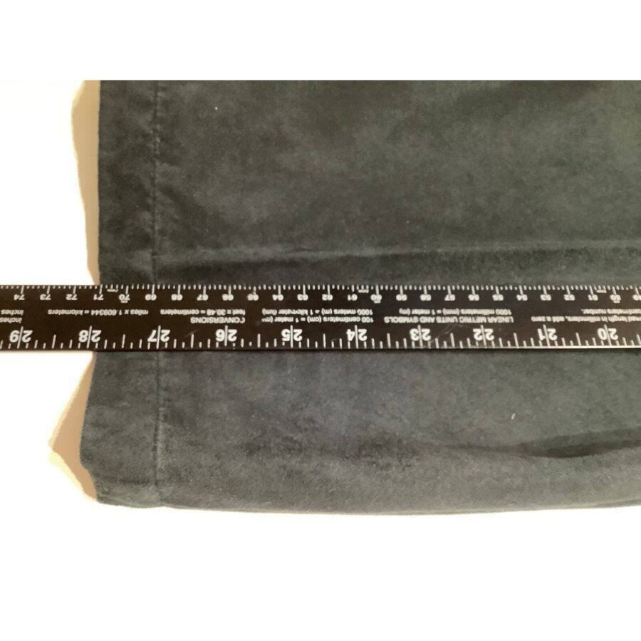 A black garment is measured with a black ruler showing both inches and centimeters, placed horizontally across the fabric on a white surface.