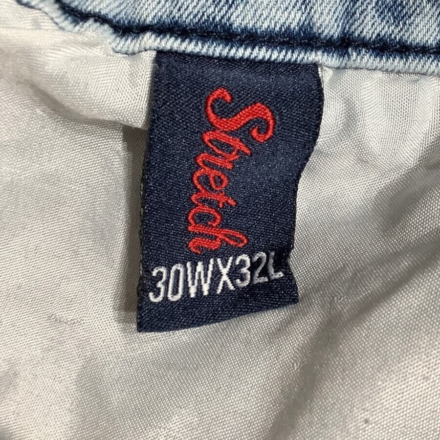 A clothing label on a fabric background displays "Stretch" with size 30WX32L, indicating waist and length measurements for jeans or pants.