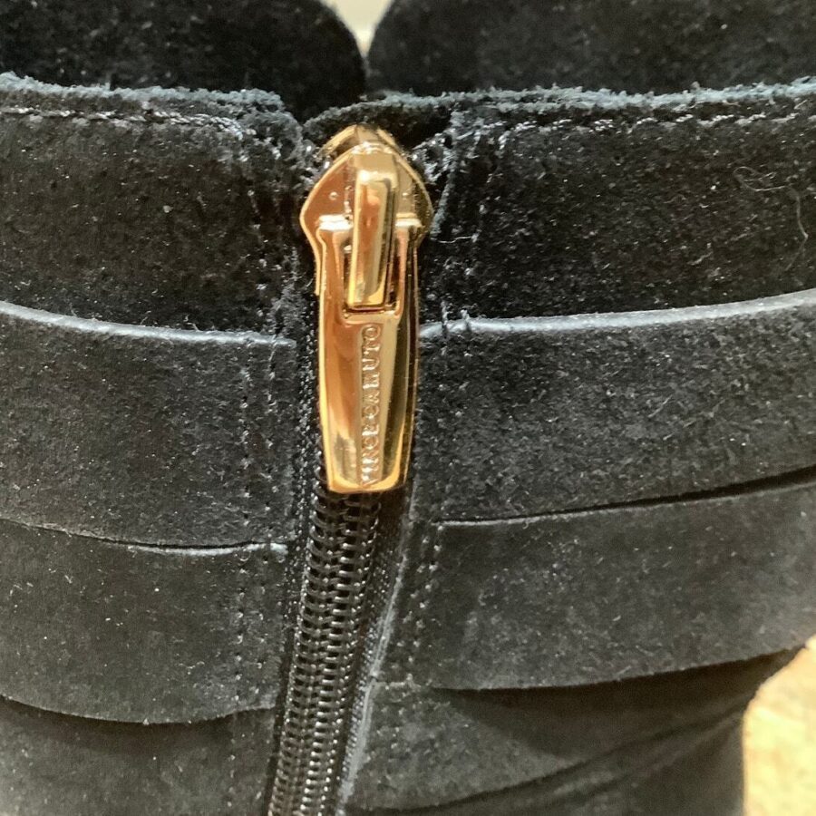 Close-up image of a black suede boot with a gold-colored zipper and the brand label "MICHAEL KORS" engraved on it.