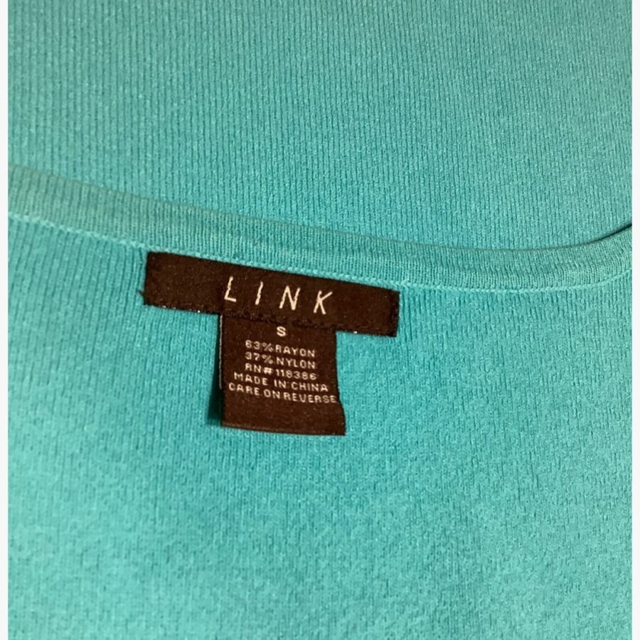 A close-up of a teal fabric with a black label showing "LINK" and garment care instructions. No landmarks or historical buildings visible.