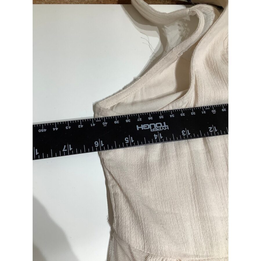 A light-colored fabric garment with a black ruler placed across it, measuring approximately 13 inches (33 cm) horizontally, is displayed on a white surface.