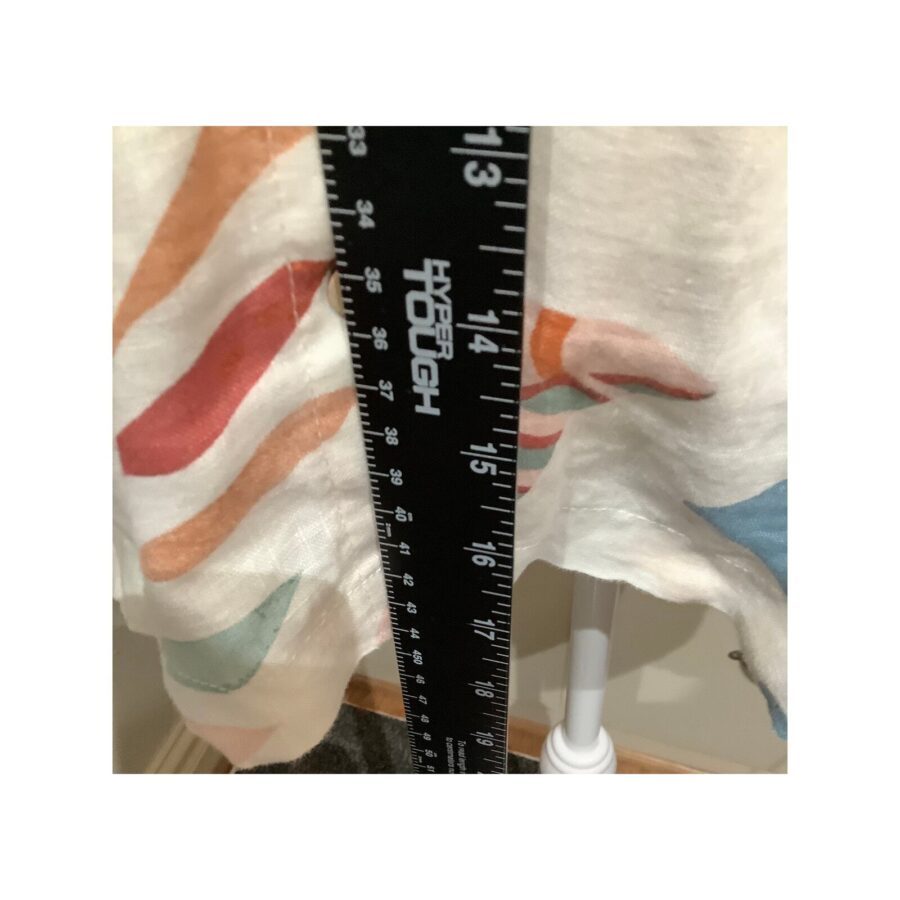 A black measuring tape is held against a fabric with a colorful pattern, indicating a measurement of approximately 15 inches.