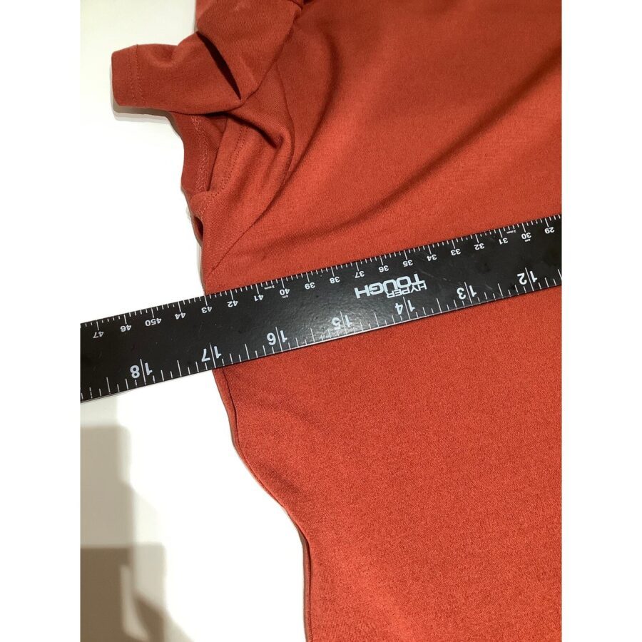 A black ruler is placed diagonally across an orange fabric, showing measurements in both inches and centimeters. The fabric is slightly crumpled.