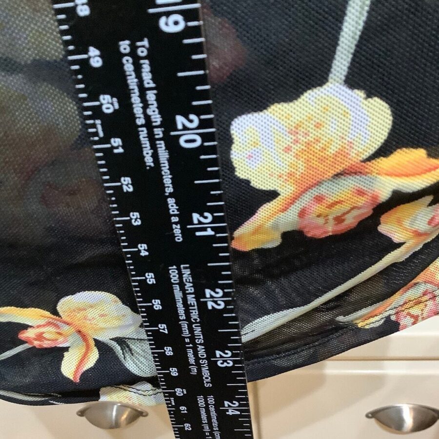 A fabric with a floral pattern is measured using a black ruler marked in inches. The background is partially visible with drawer handles.