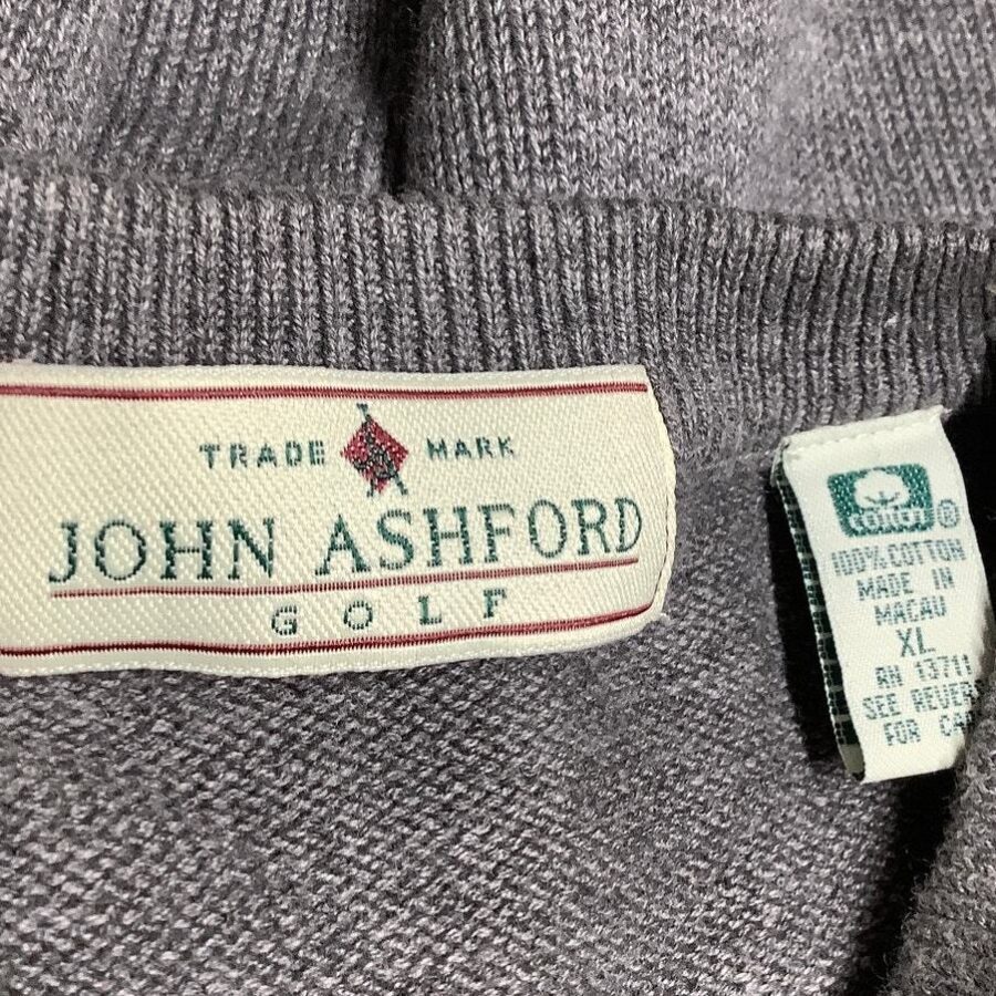 A grey John Ashford Golf sweater with two labels: one indicating the brand and the other providing care instructions, stating it's made in Macau.