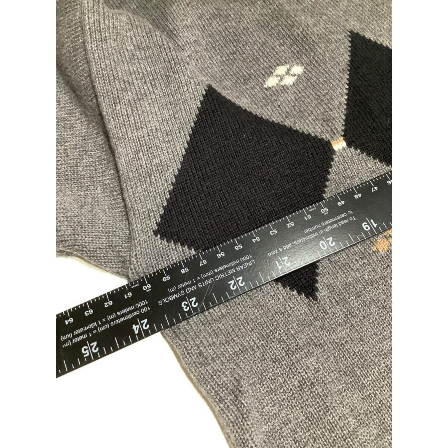 A ruler measuring a gray, knitted fabric with black triangle patterns and a small, white stain. The fabric appears to be a sweater.