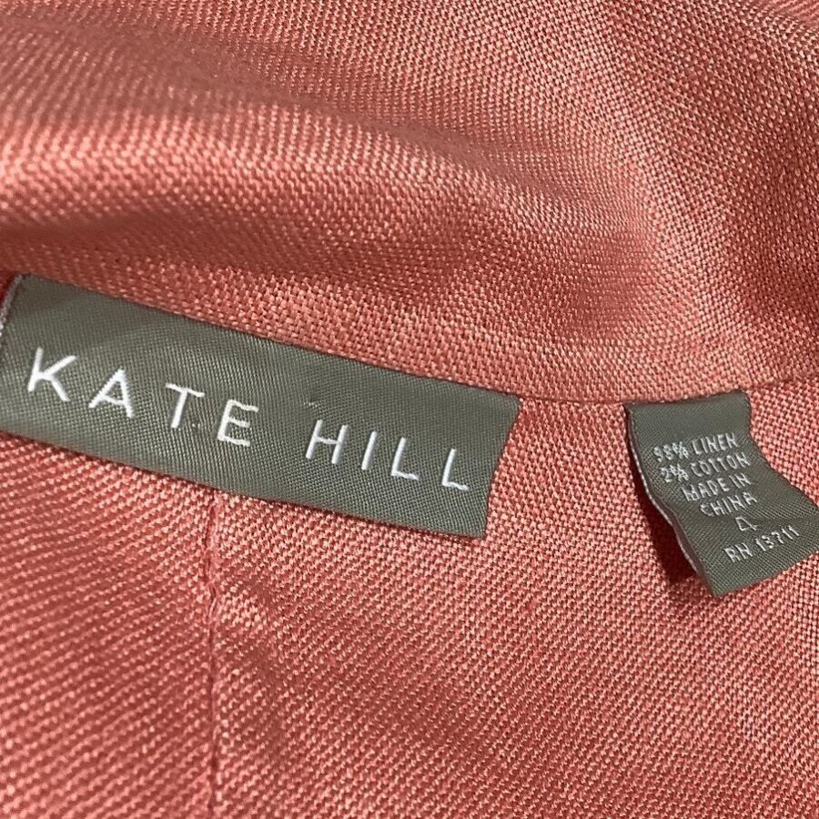 A close-up of a pink fabric with "KATE HILL" and care labels indicating it is 98% linen, 2% cotton, and made in China.