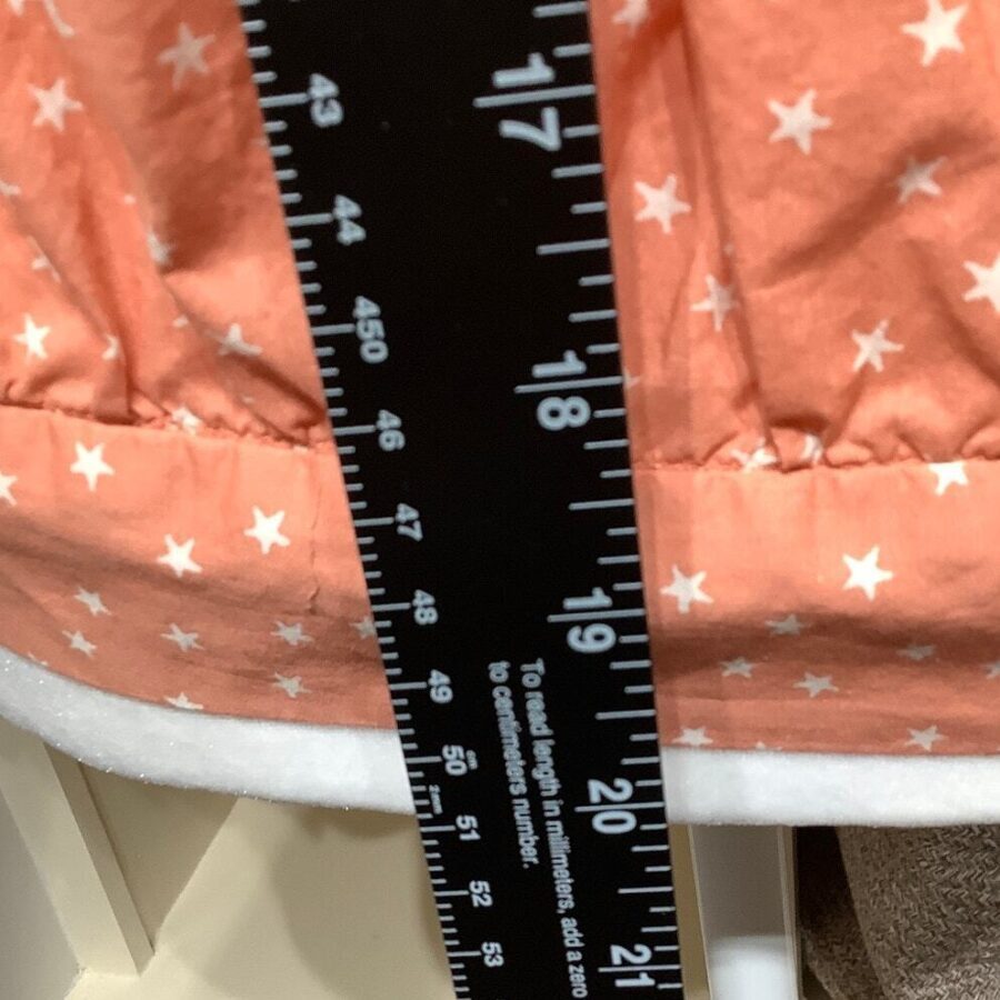 Close-up of a peach-colored fabric with white stars, next to a black ruler with white markings showing measurements in inches.