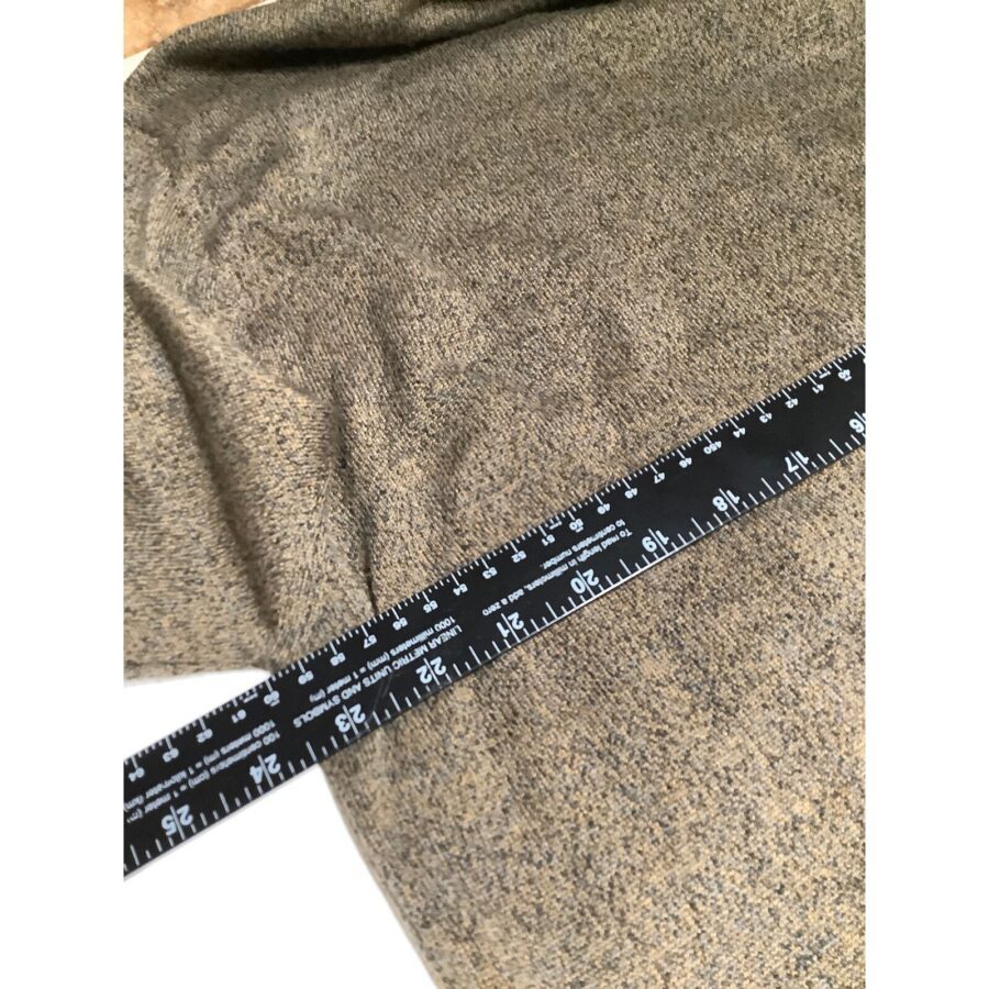 A black measuring tape is placed on a beige textured fabric, showing measurements in inches and centimeters, indicating the fabric's dimensions.