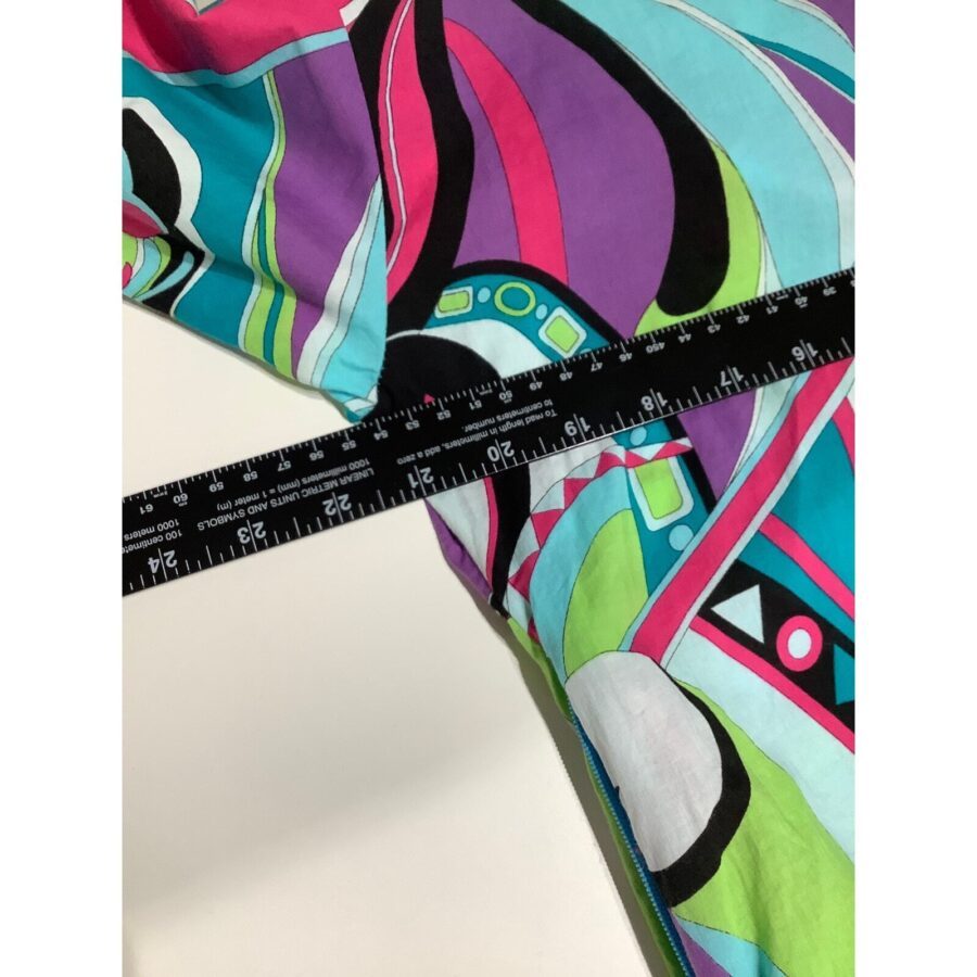 A colorful fabric with abstract patterns and a black ruler placed diagonally across it, showing measurements in inches and centimeters.