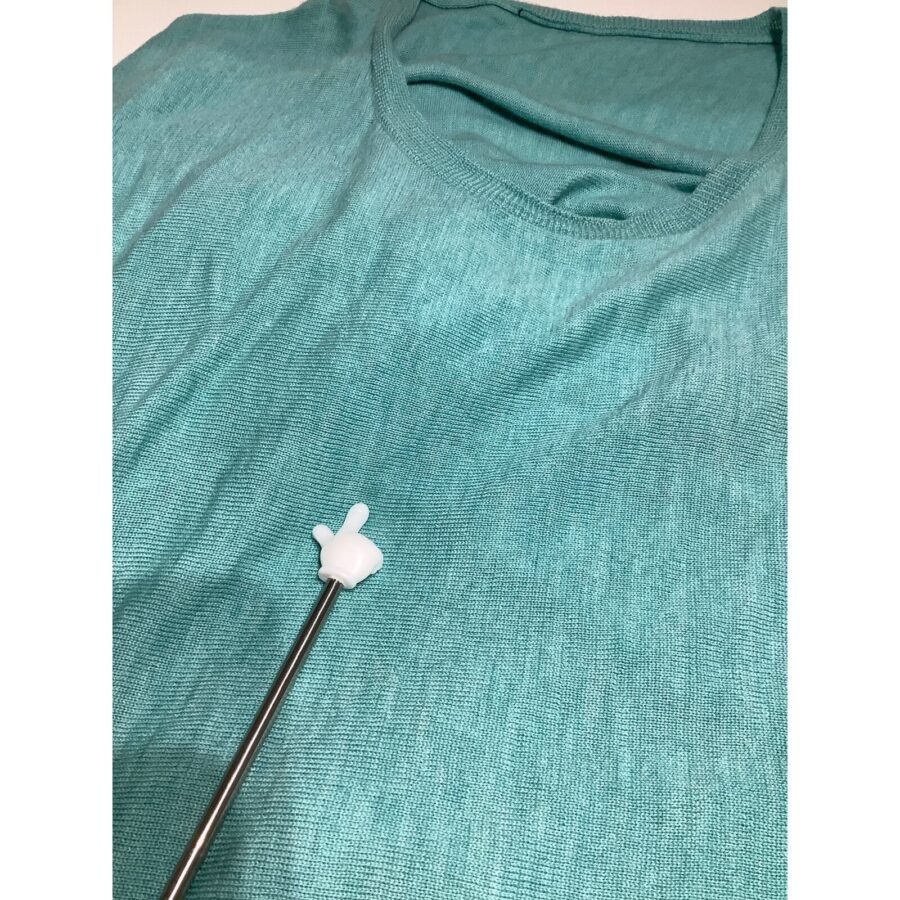 A teal shirt is displayed with a metal pointer, tipped with a white glove-shaped end, indicating a spot on the shirt's fabric.