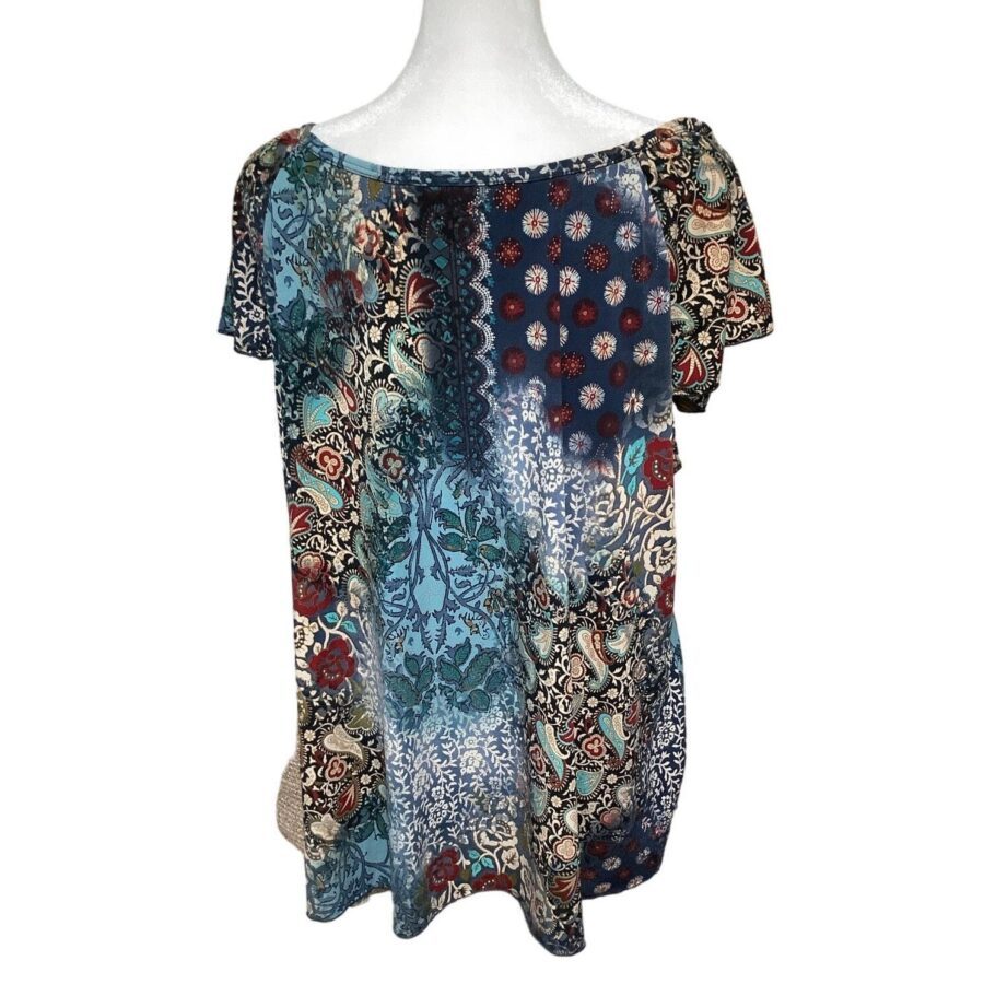 A multicolored short-sleeve blouse with various intricate patterns displayed on a white mannequin torso. The blouse features floral and abstract designs.