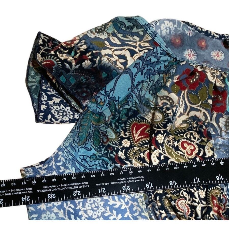 A close-up image of a colorful, patterned fabric with a black ruler for scale. The design includes floral and abstract elements in blue, red, and green.