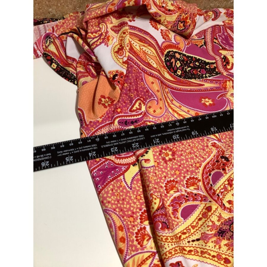 A pink and orange patterned fabric is being measured with a black ruler on a white surface, displaying a vibrant paisley design.