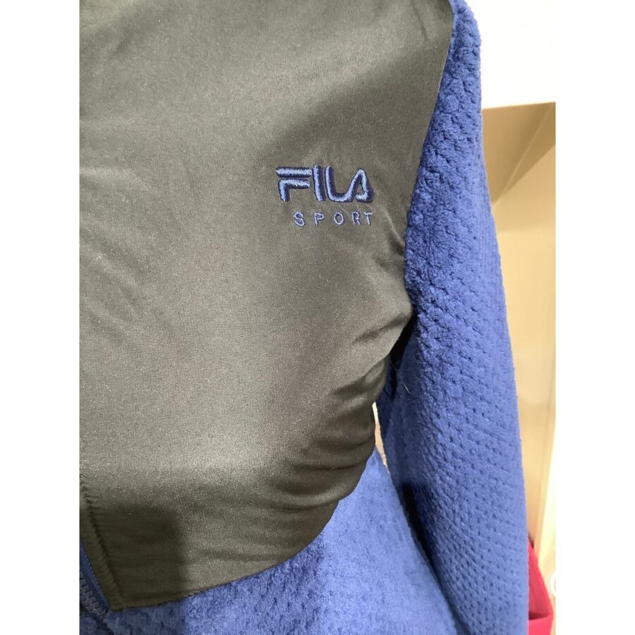 A close-up image of a jacket with Fila Sport branding, featuring blue textured sleeves and a dark green front section.