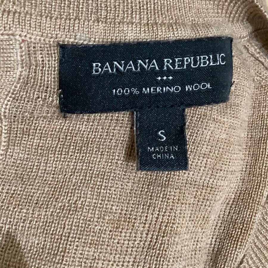 A close-up of a beige garment showing a black label that reads "BANANA REPUBLIC 100% MERINO WOOL, S, MADE IN CHINA."