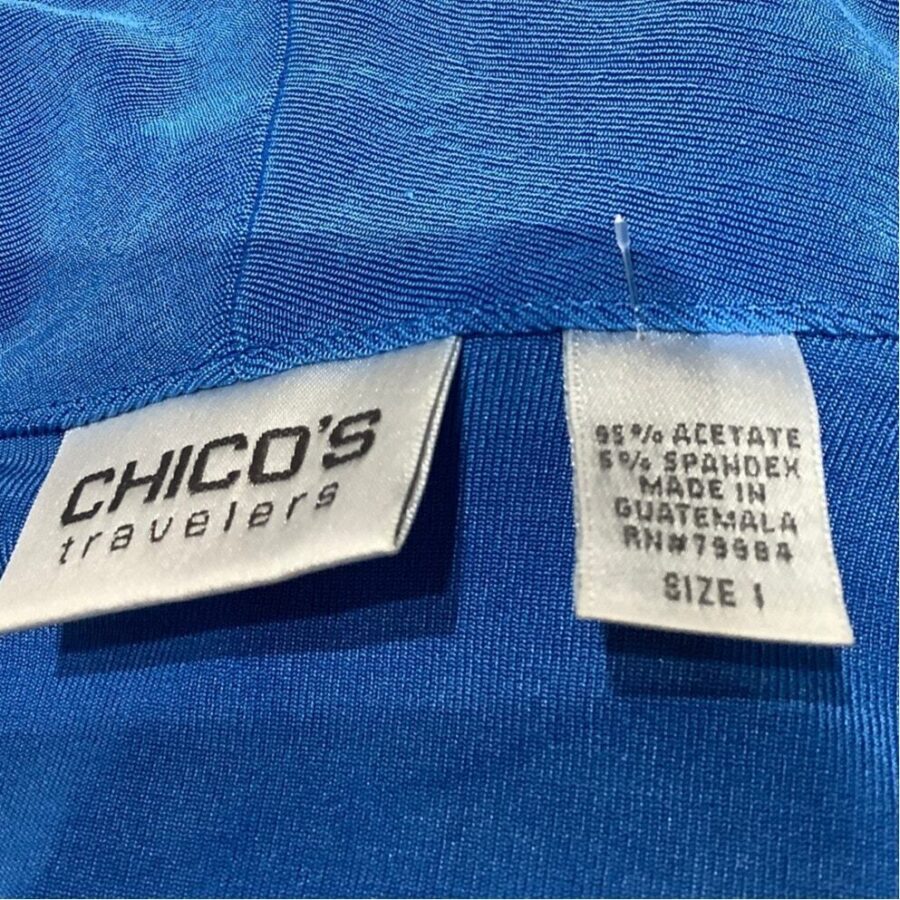 Two clothing tags on a blue fabric. Labels read "CHICO'S Travelers" and "Made in Guatemala" with material composition and size details.