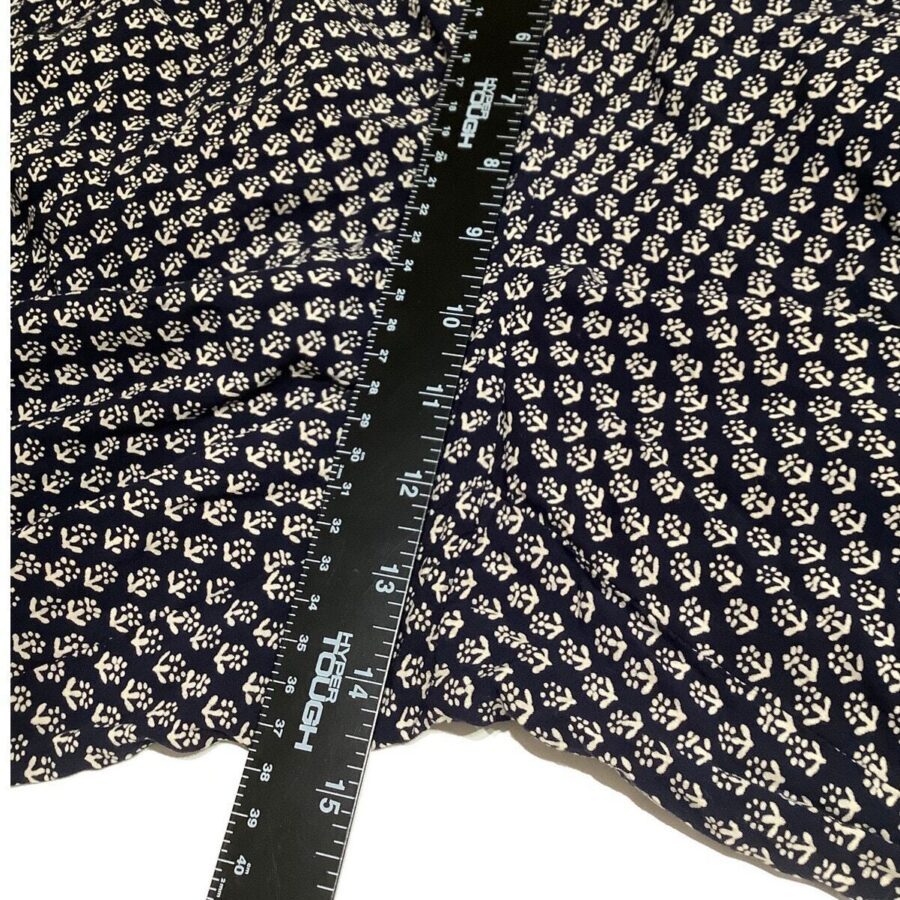 A black and white patterned fabric is measured with a black ruler displaying both inches and centimeters, positioned diagonally across the material.