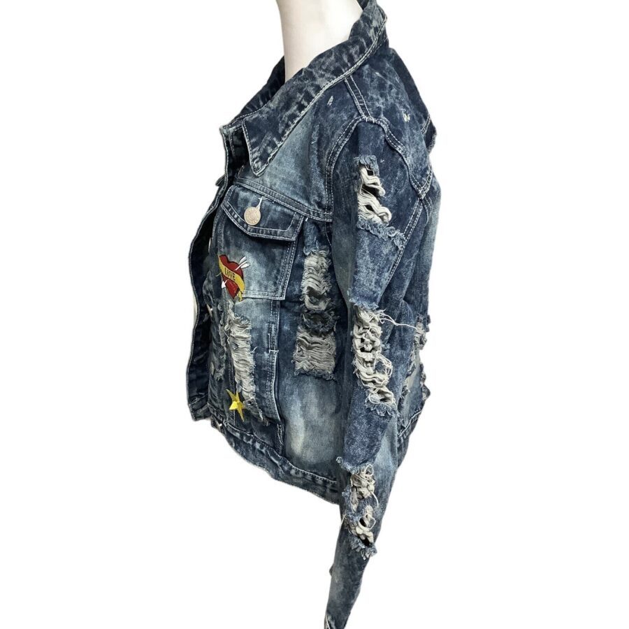 A distressed denim jacket adorned with colorful patches is displayed on a mannequin, featuring extensive rips and a worn texture.