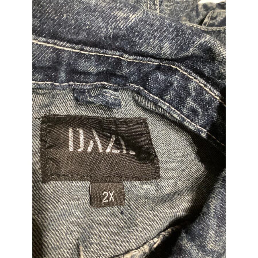 Close-up of a denim jacket's interior label showing "DAZR" and size "2X." The fabric has a faded, worn texture with visible stitching details.