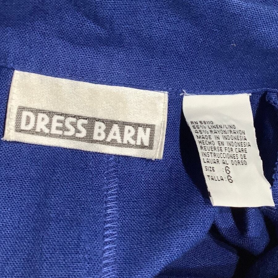 The image shows clothing tags on a blue fabric, with one tag displaying the brand "Dress Barn" and the other indicating size and care instructions.