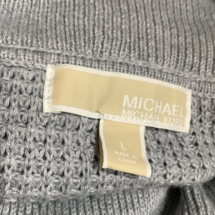 A close-up image of a grey knitted garment with a label that reads "MICHAEL MICHAEL KORS, L, MADE IN CHINA." No landmarks or historical buildings visible.