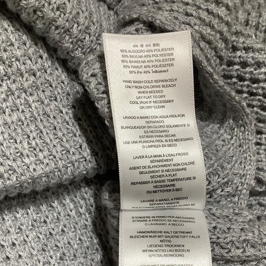 Image of a gray knitted fabric with a care instruction label. The label details washing and maintenance guidelines in multiple languages.