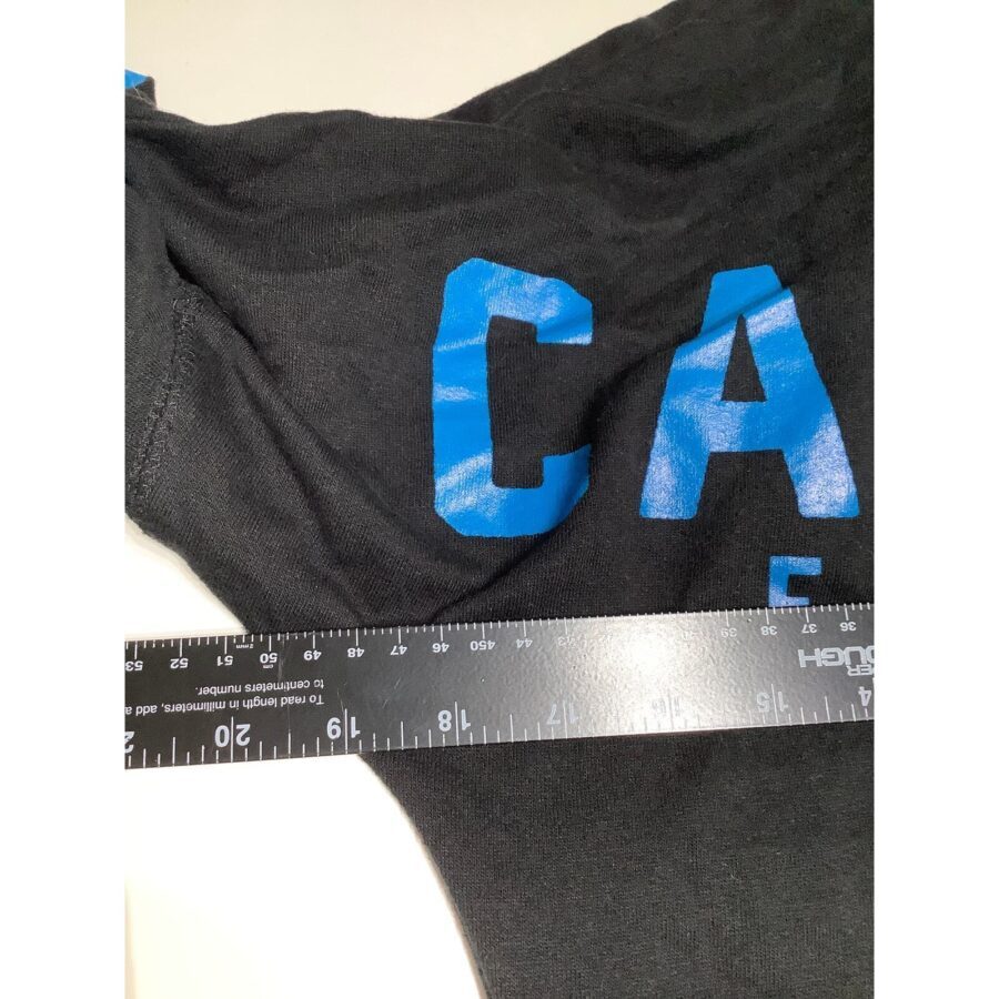 A black fabric with blue letters partially visible, measured with a clear plastic ruler showing centimeters and inches on a white background.