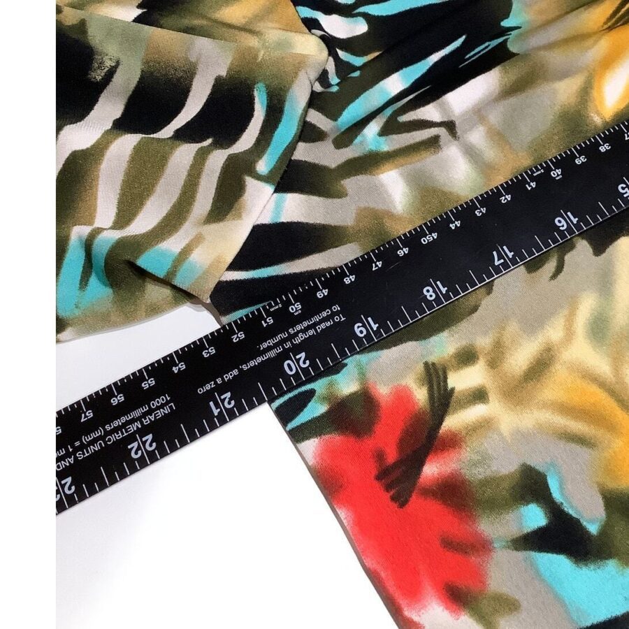 A colorful fabric with an abstract pattern is laid beneath a black measuring ruler displaying inches and centimeters.