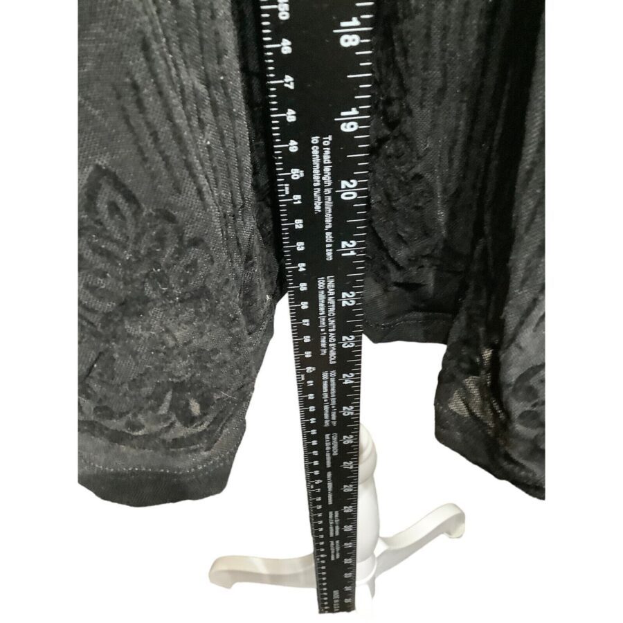 A black fabric with floral pattern is measured by a black ruler standing on a white, three-legged stand against a plain background.