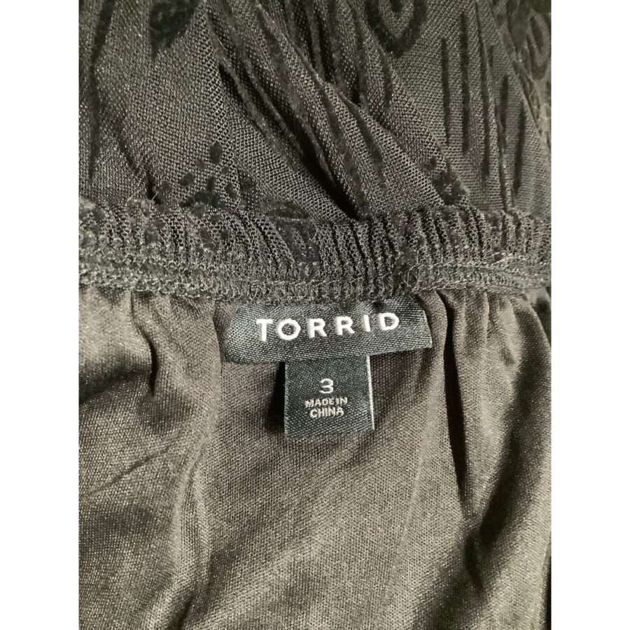 A close-up of a black garment label from the brand "Torrid," indicating size "3" and made in China, with textured material visible.