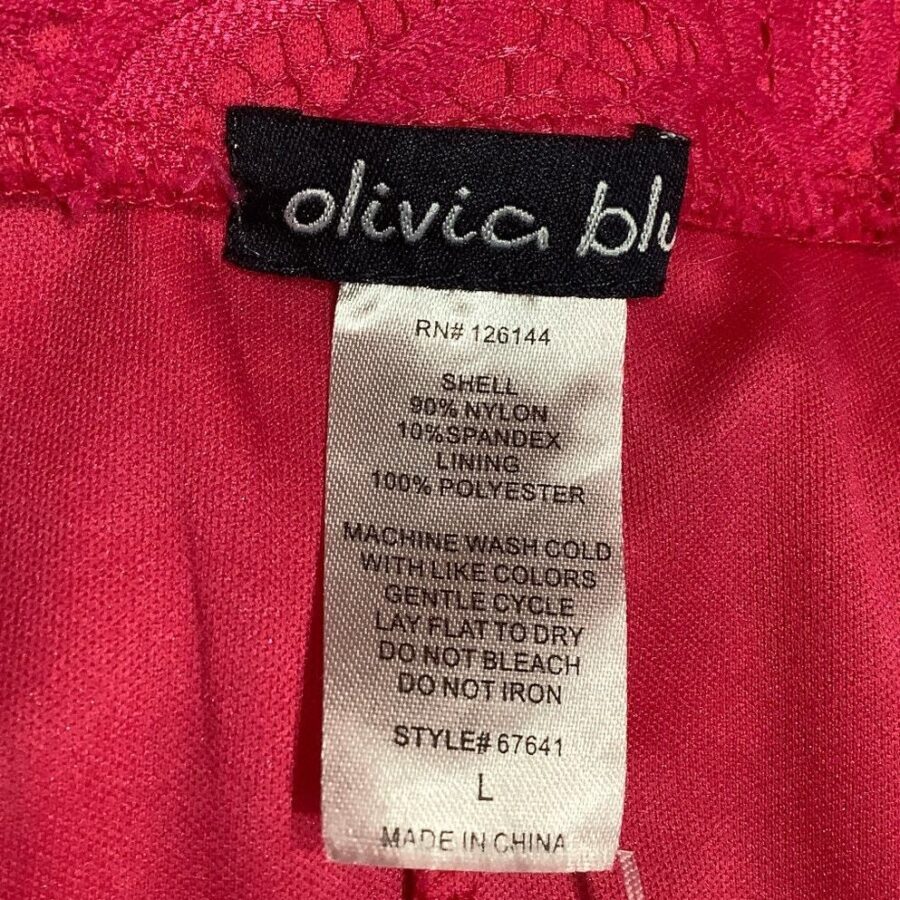 A clothing tag on a red garment showing care instructions and fabric composition. The garment is of the brand "olivia bleu," made in China.