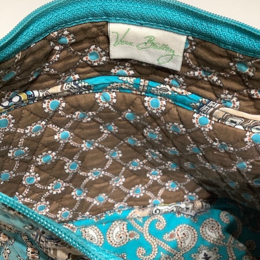 An open Vera Bradley patterned purse reveals a brown and turquoise interior with various pockets and an embroidered logo on a fabric tag.