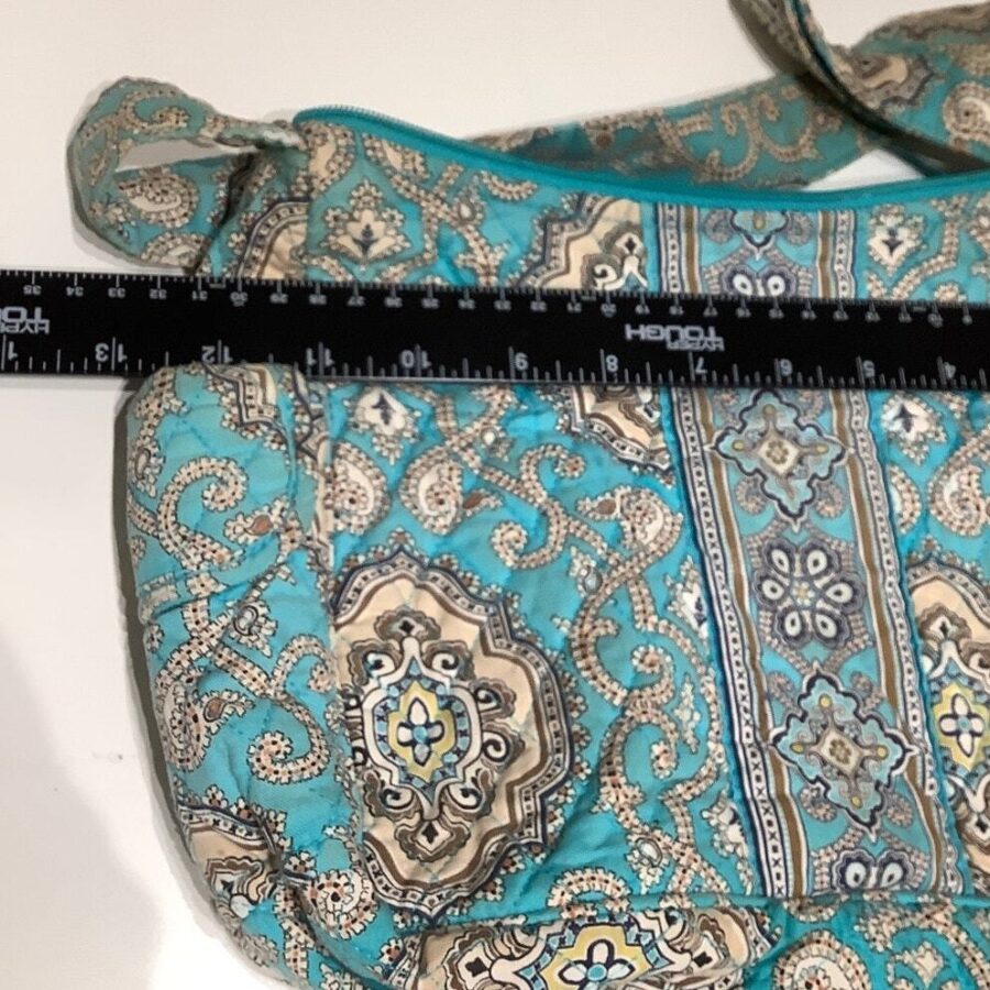 A turquoise patterned fabric bag with a strap and a black ruler placed on top, indicating measurements on a white background.