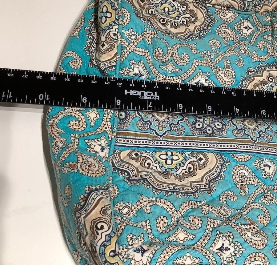 A blue paisley-patterned fabric partially covered by a black ruler marked in inches, lying on a white, flat surface.