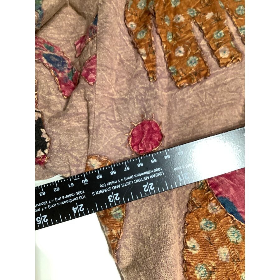 A close-up of colorful, patterned fabric with an elephant design. A black ruler is placed across the fabric for measurement.