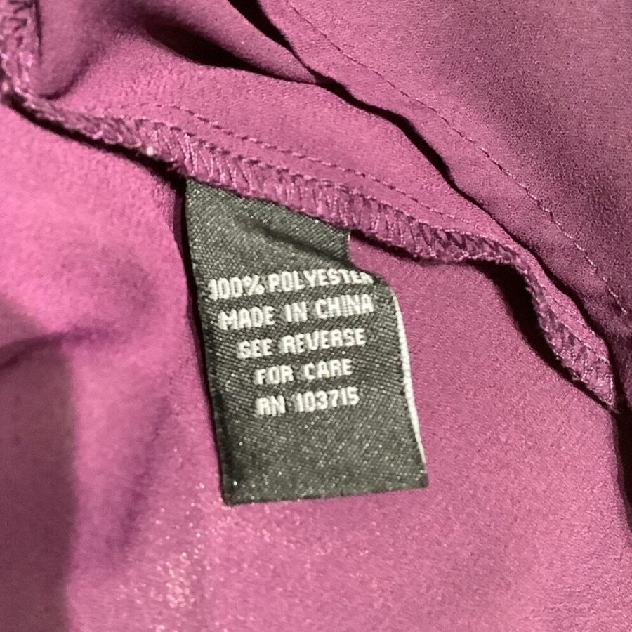 A clothing label on a purple fabric reads “100% Polyester, Made in China, See Reverse for Care, RN 10371S.” showing manufacturing details.