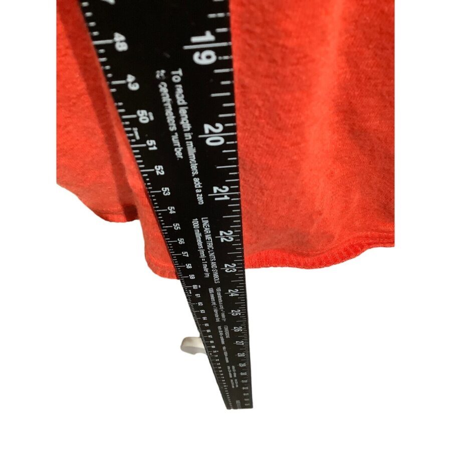 A black ruler measuring a red fabric, showing both metric and imperial units. The image focuses on the measurement markings and fabric detail.