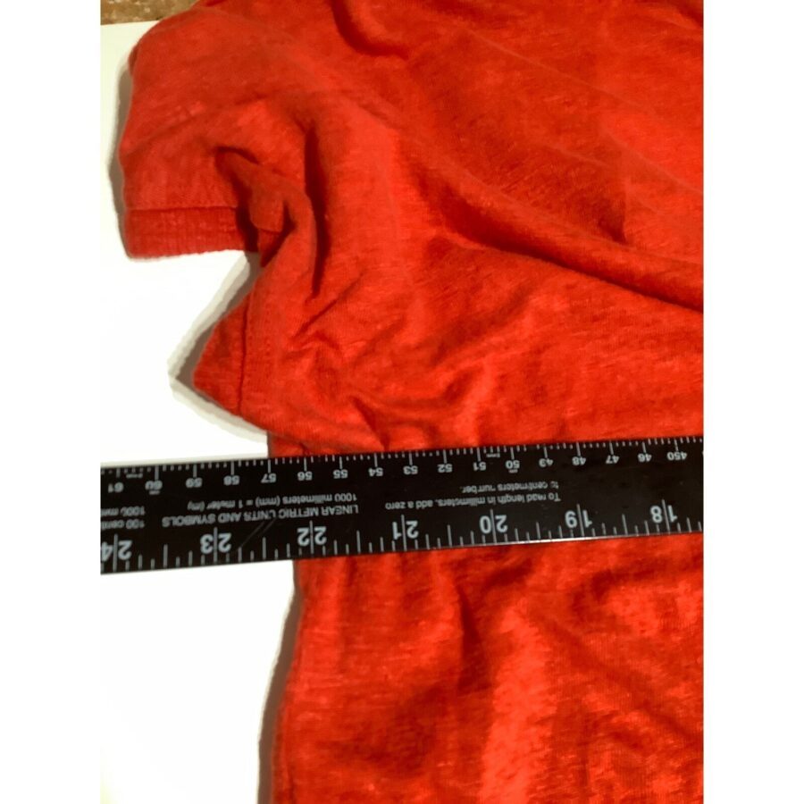 A red fabric is laid out with a black measuring tape placed diagonally across it, displaying measurements in inches and centimeters.