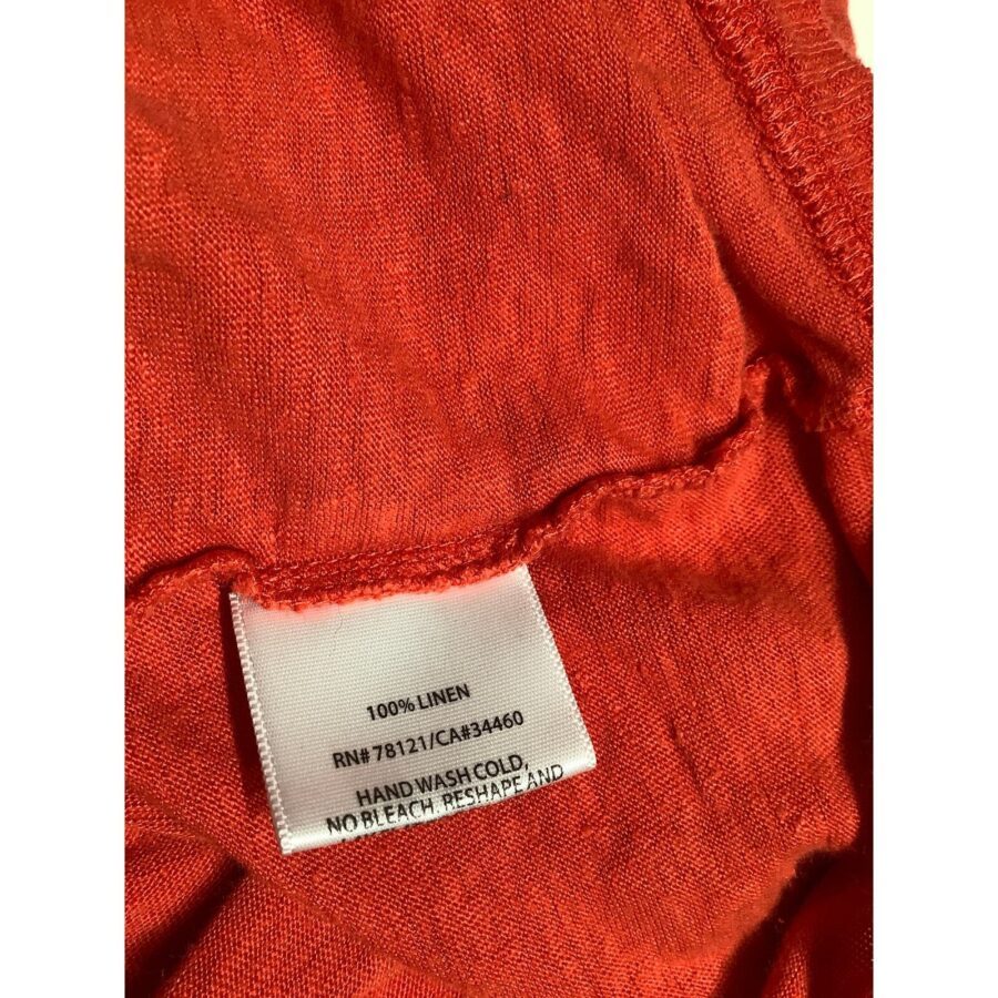 A close-up of a red linen fabric with a care label, showing washing instructions and material composition. Label reads: "100% Linen, Hand Wash Cold."