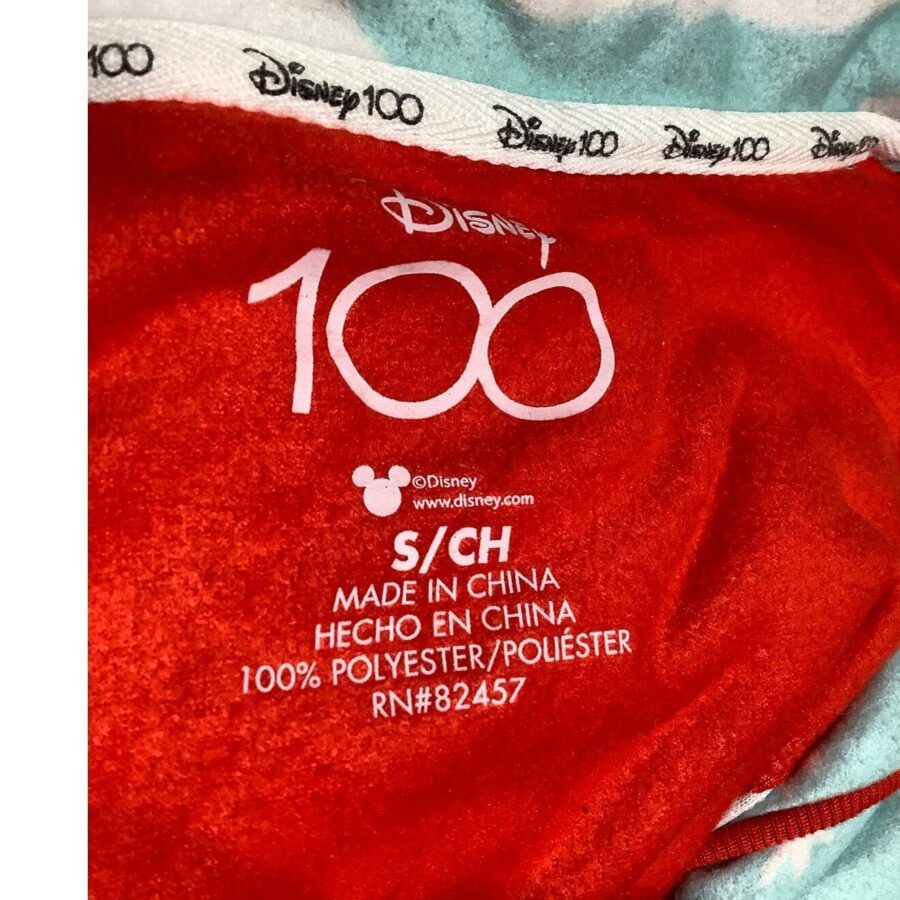 A red Disney 100 fabric label showing size S/CH, made in China, composed of 100% polyester, with a Disney logo and website.