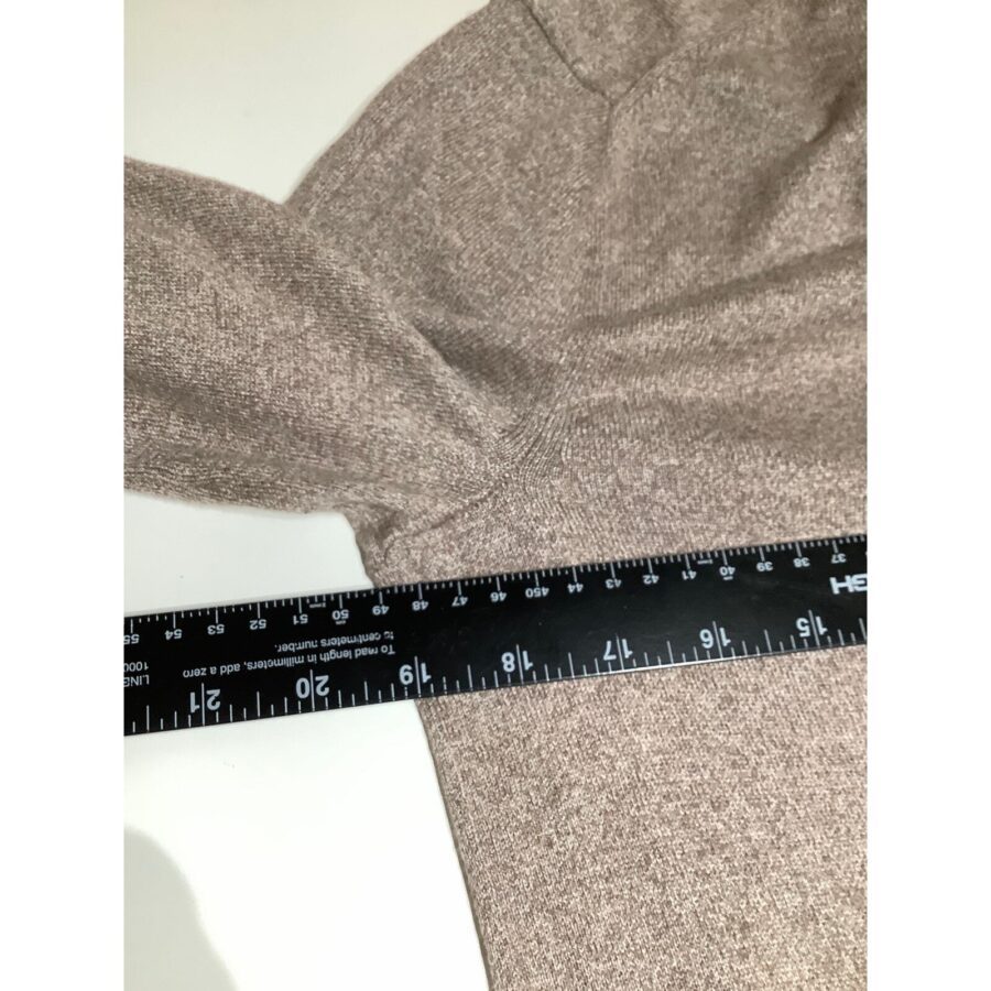 A measuring tape is placed across the sleeve of a brown knitted garment on a white surface, indicating precise measurements.