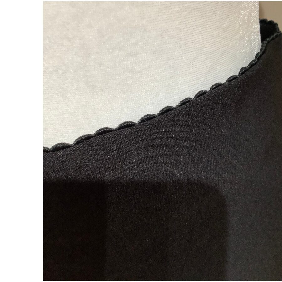 Close-up image of a black fabric with scalloped edge detail, showing contrast against a lighter background. No landmarks or historical buildings visible.