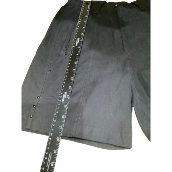 A pair of black shorts with a zipper pocket is displayed next to a 36-inch measurement ruler on a white surface.